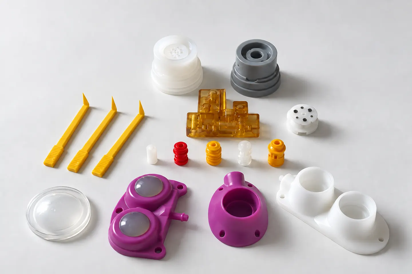 ADMO Plastique: Teile für Beatmungsgeräte, eine Pumpe, ein durchscheinendes bernsteinfarbenes Teil, Katheterteile und kleine farbige Bauteile, zusammen abgebildet.
